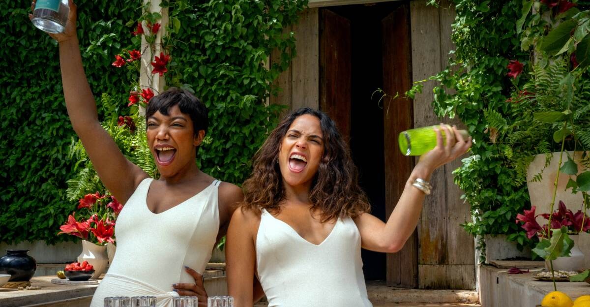 Two women holding drink shakers and screaming happily in Blink Twice.