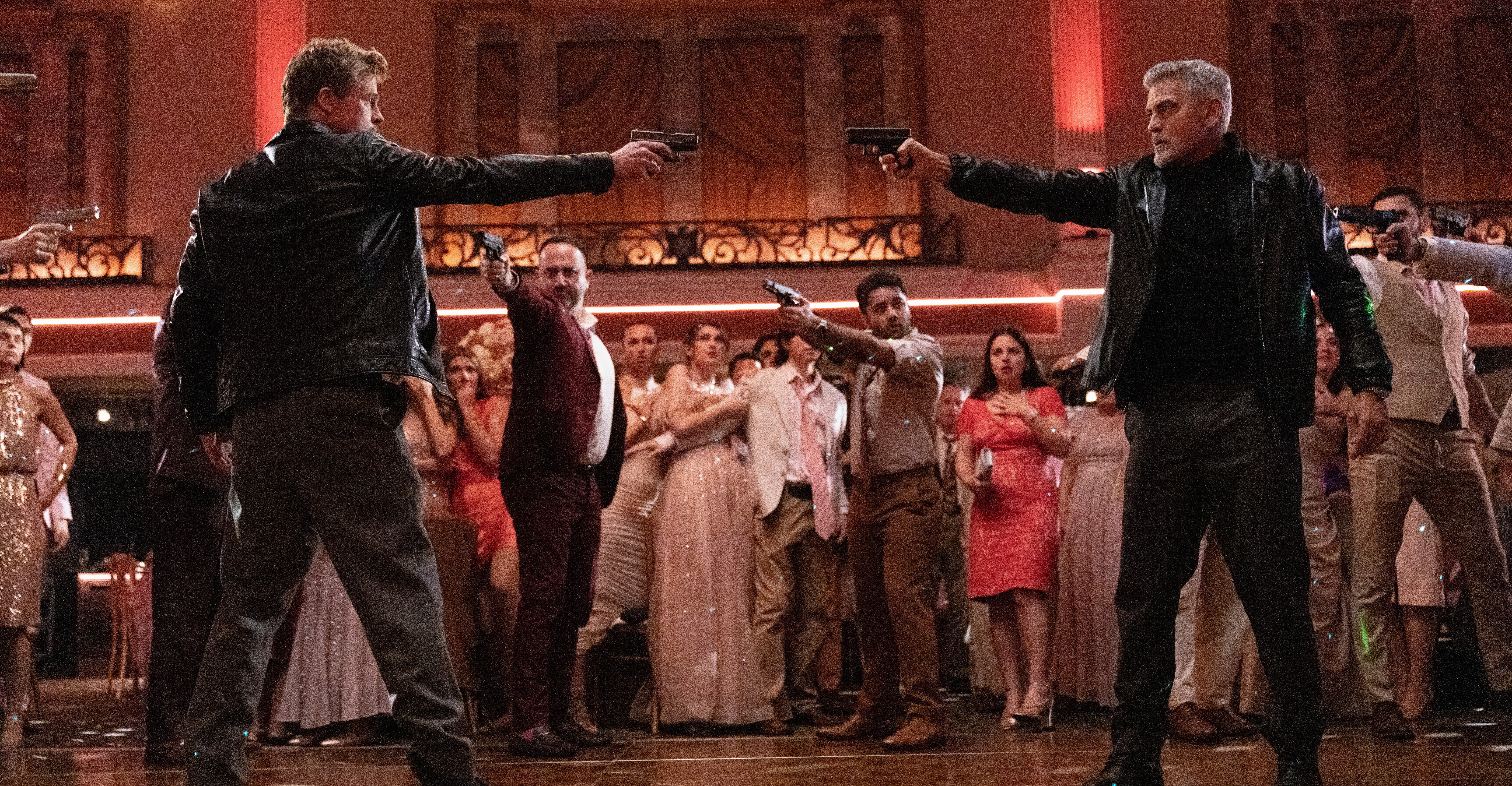 Brad Pitt and George Clooney pointing pistols at one another while other people point guns at them on a dance floor in Wolfs.