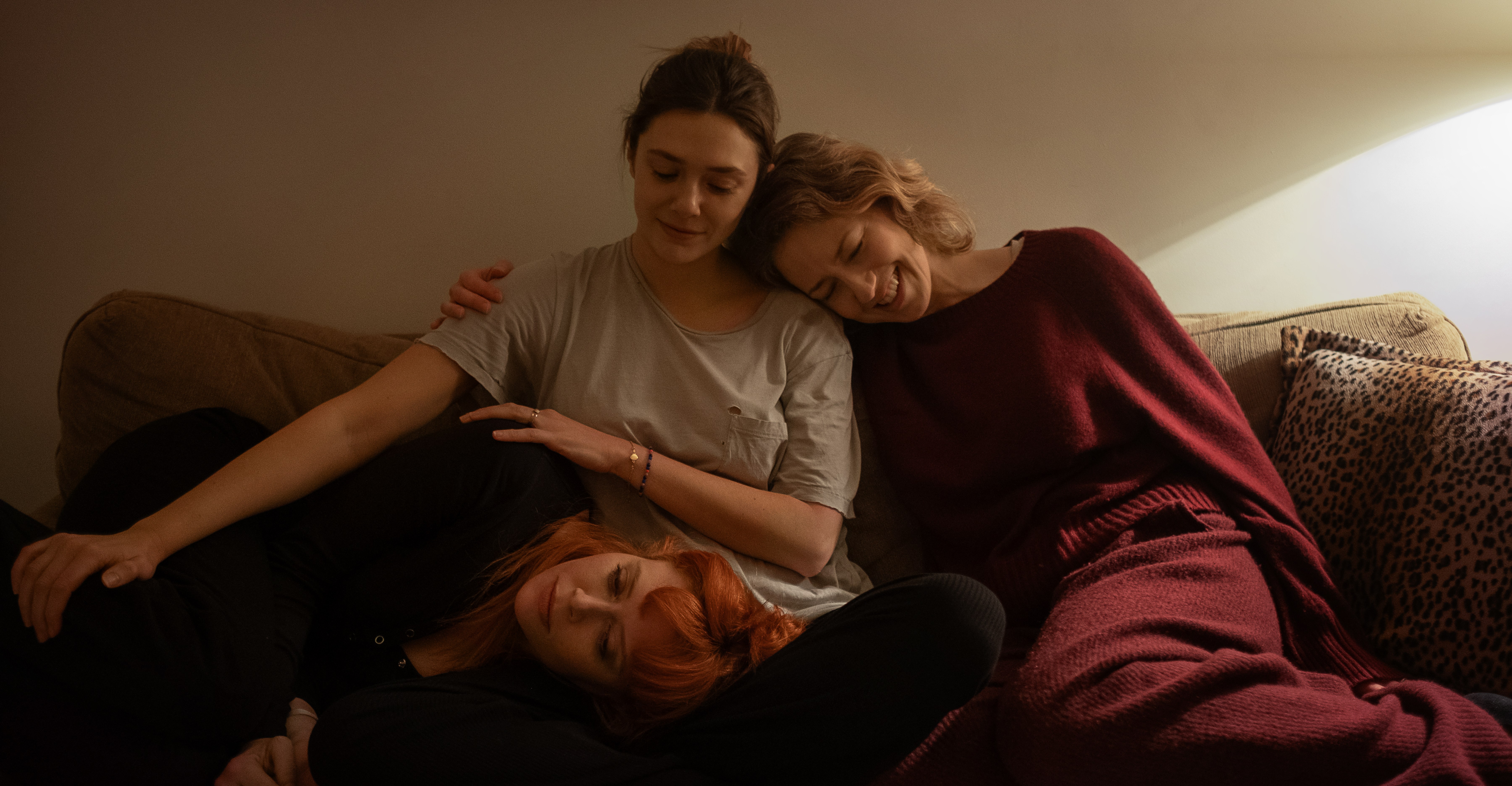 Natasha Lyonne, Elizabeth Olsen, and Carrie Coon sitting on a couch in His Three Daughters.