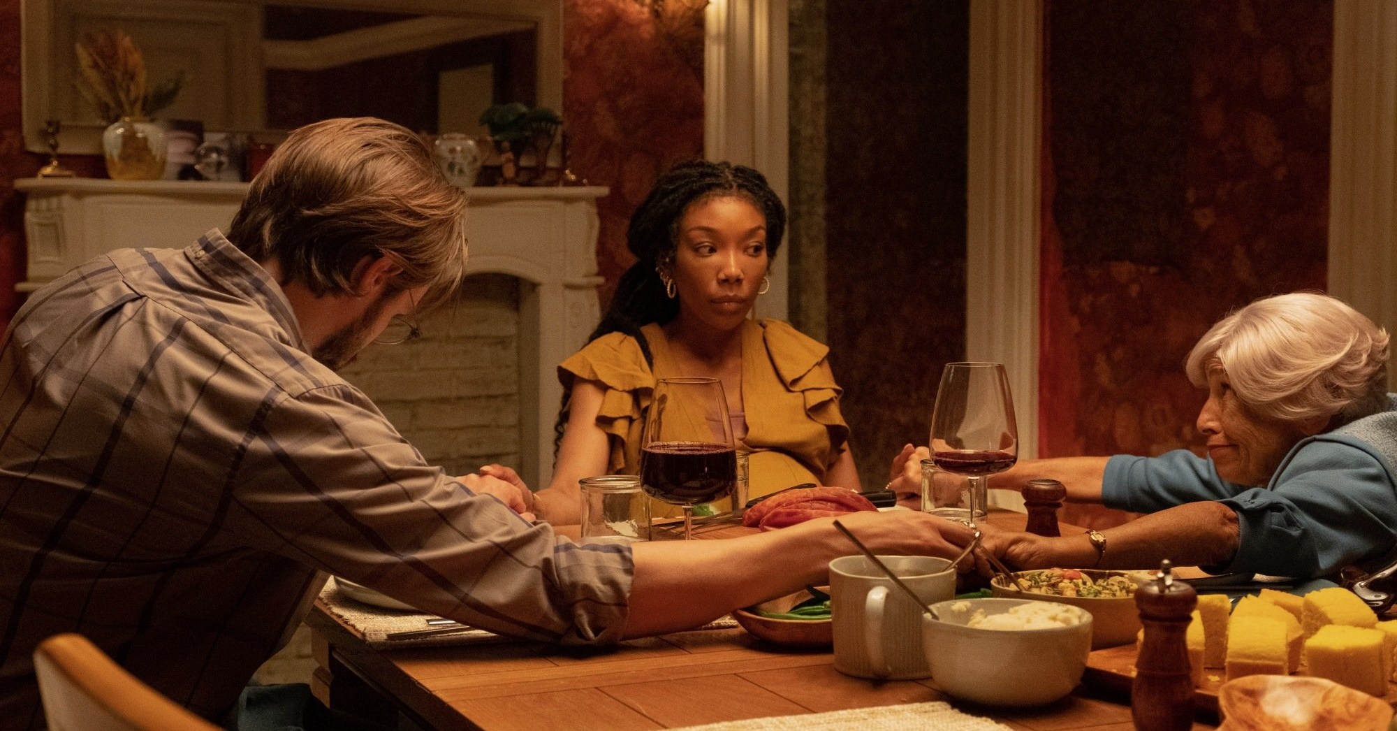 Brandy Norwood sitting at a table and holding hands with a bearded man and an elderly woman in The Front Room.