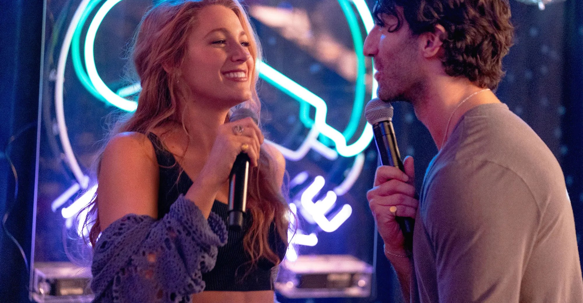 Blake Lively and Justin Baldoni holding microphones in It Ends With Us.