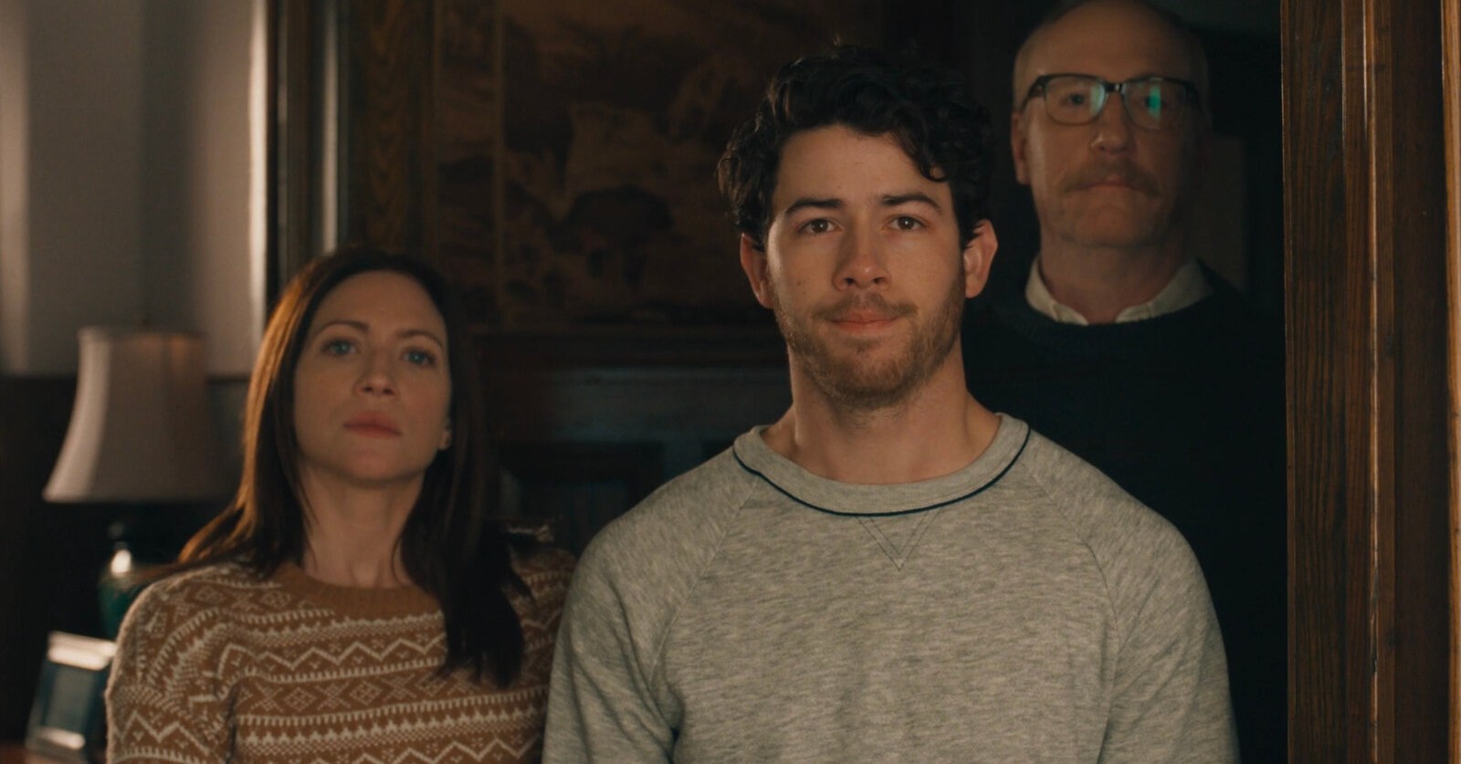 A man standing in a door frame in front of an older man and woman in The Good Half.