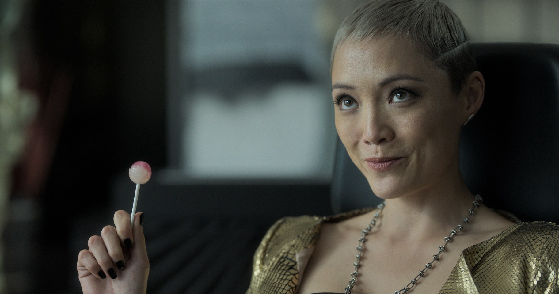 Pom Klementieff smirks with a pink lollipop in her hand in The Killer’s Game