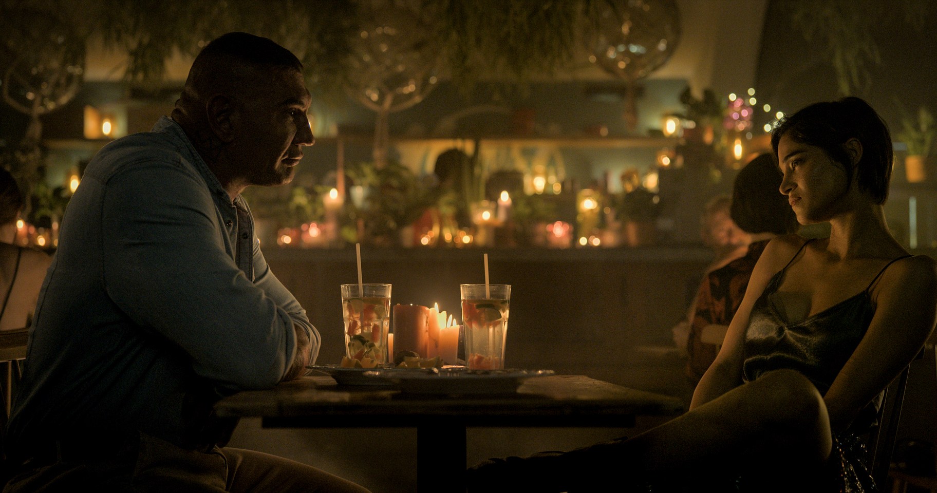 Dave Bautista and Sofia Boutella sit together at a table on a dinner date in The Killer’s Game