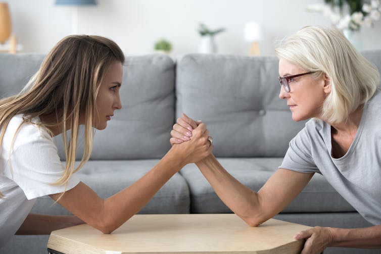 Two women of different generations arm wrestle.