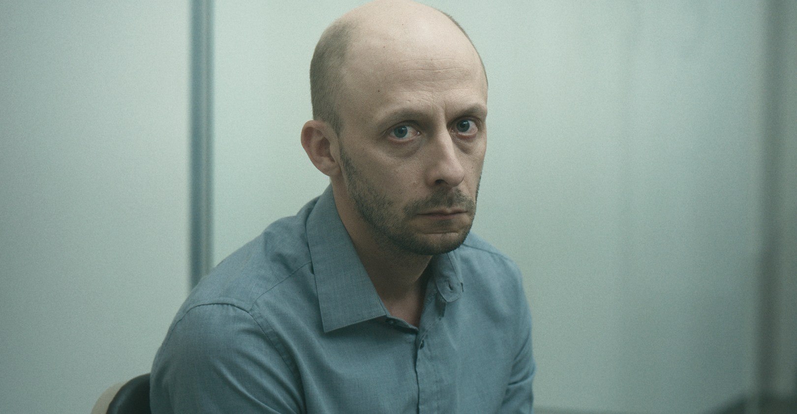 Chevalier, a bald man with a death stare, looks into the camera in Red Rooms 