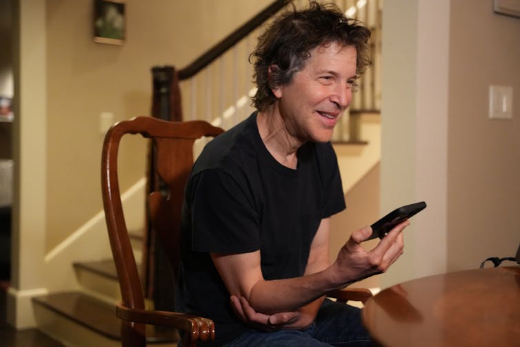 smiling seated man holds cell phone in his hand for a speaker call