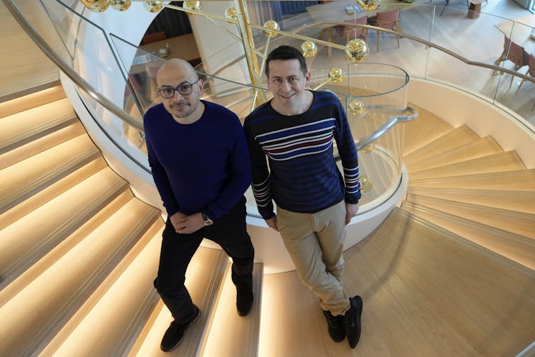 two men on spiral staircase look up at camera