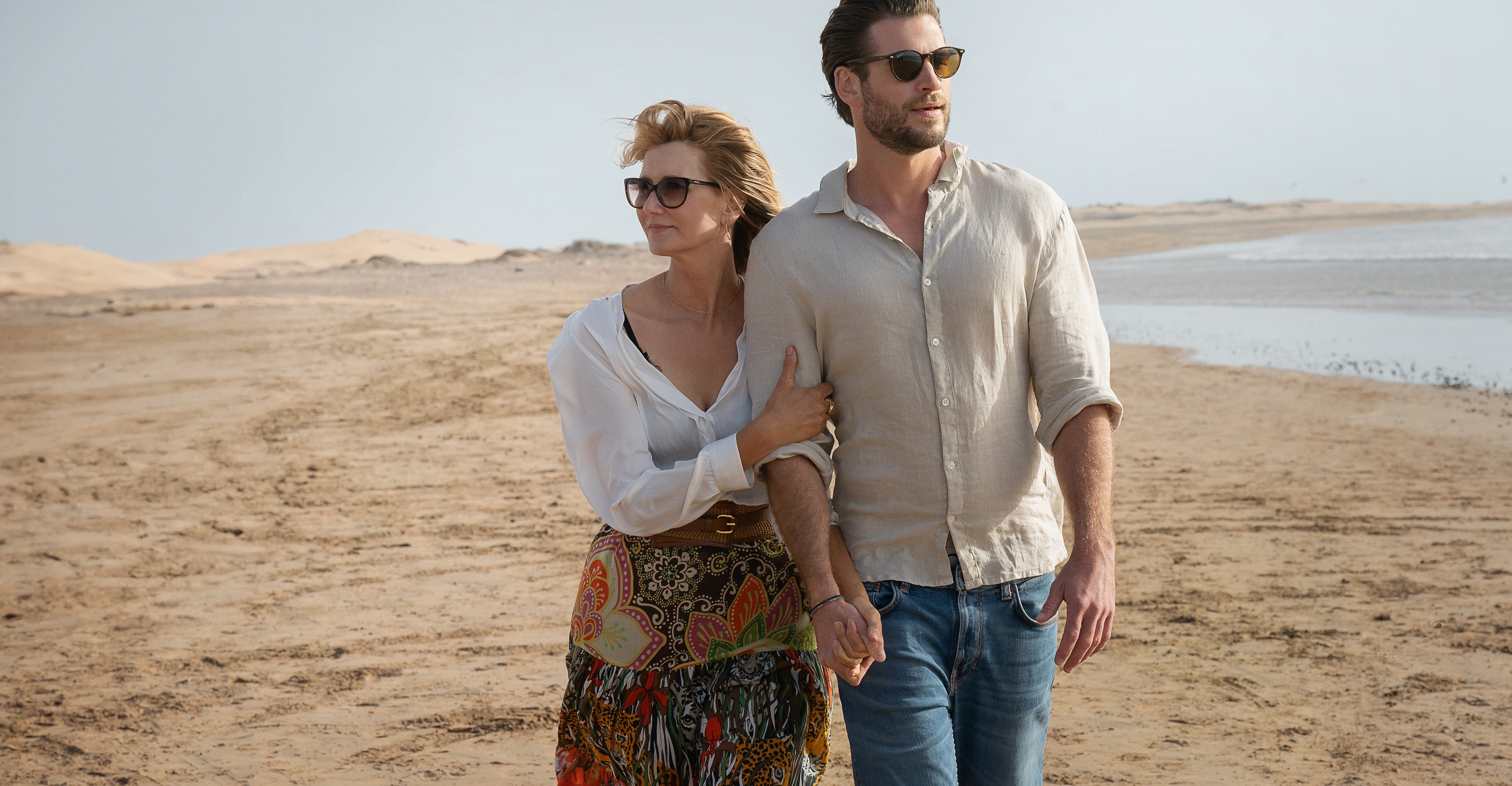 A woman (Laura Dern) and a man (Liam Hemsworth) walking hand-in-hand along a shore in Lonely Planet.