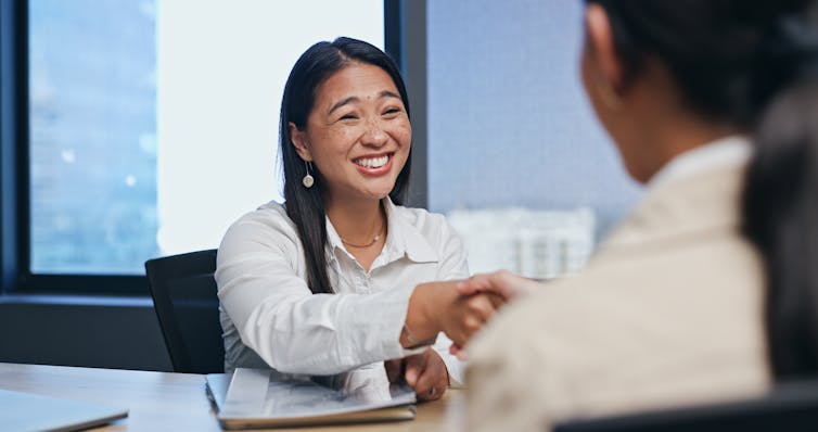 A young woman smiling while shaking hands with someone who has their back to the camera