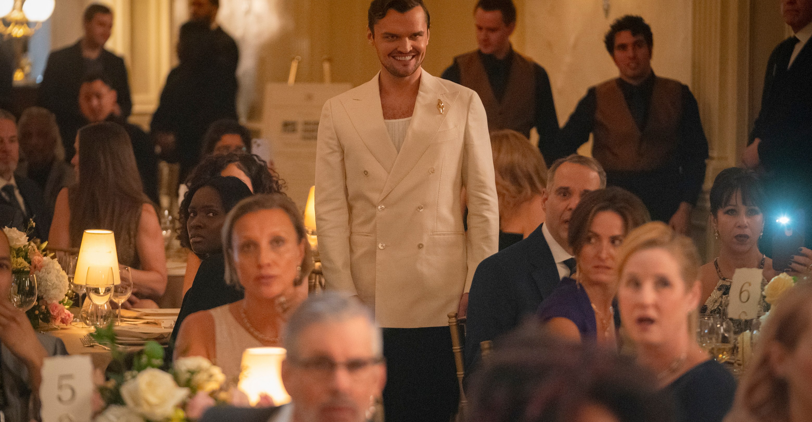 Ray Nicholson stands up at a black tie event wearing a white jacket and a sinister grin on his face in Smile 2 