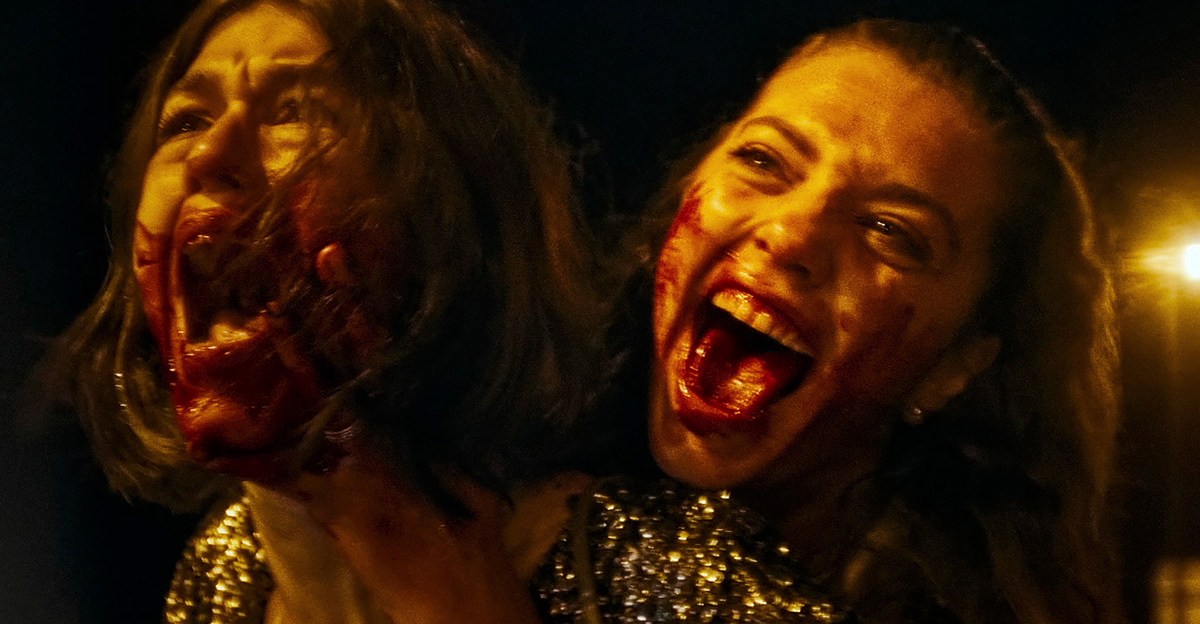 Two women with blood-splattered faces screaming in MADS.