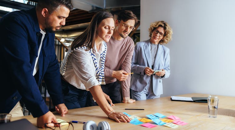 A group of business professionals looking down at sticky notes on a table while having a discussion