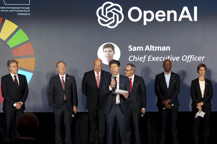 A group of people in suits stand together under the words 'OpenAI' and 'Sam Altman, Chief Executive Officer'