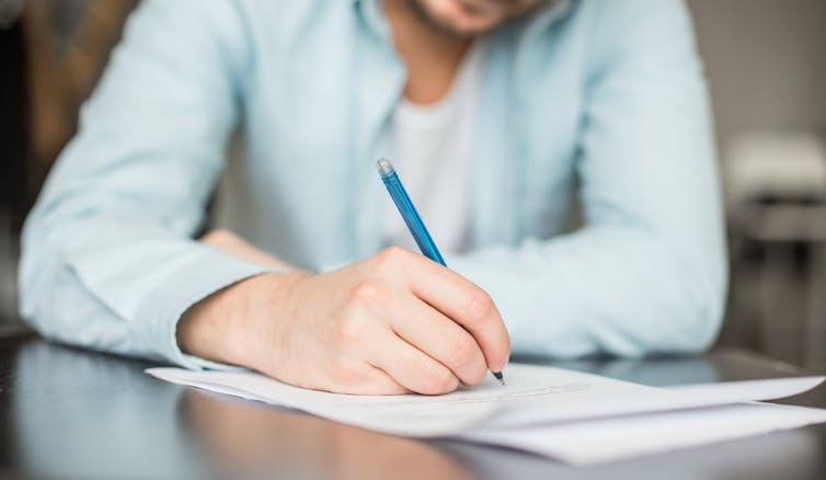 A man writes on a sheet of paper.