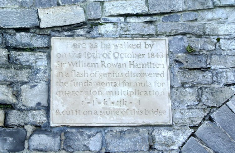 Photo of a plaque with inscription 'Here as he walked by on the 16th of October 1843 Sir William Rowan Hamilton in a flash of genius discovered the fundamental formula for quaternion multiplication i²=j²=k²=ijk=-1  & cut it on a stone of this bridge.'