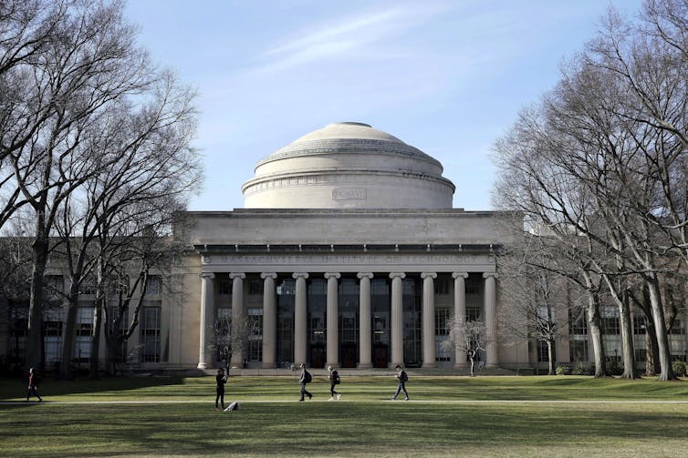 a large gray building with columns and a dome and a lawn with trees on either side